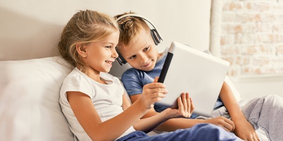 Kinder mit Tablet und Kopfhörer auf dem Sofa